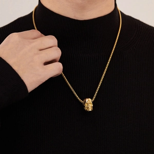 Detail of a shiny gold skull pendant on a box chain over a black turtleneck sweater