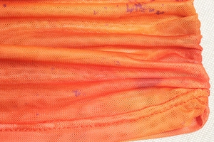 Detail of orange mesh fabric featuring irregular purple dot print and textured grid weave