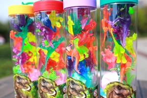 Close-up of four tubes containing colorful mini toy dinosaurs and green plants in a park