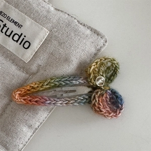 Macro shot of rainbow crochet hair clip with metal logo charm on canvas background