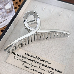 Close-up of a silver shark hair claw clip with a sleek metallic finish in a beige box