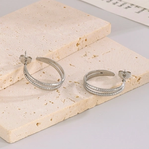Detail of silver C-shaped wheat pattern earrings on beige stone and paper background