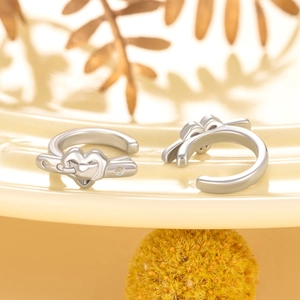 Silver heart buckle ear clips with arrow design on decorative warm yellow ceramic tray