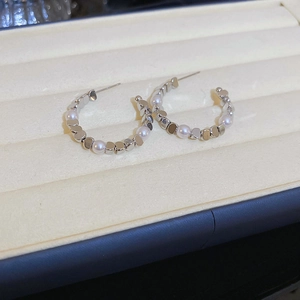 Close-up of C-shaped silver earrings with pearls and metallic squares on a velvet stand