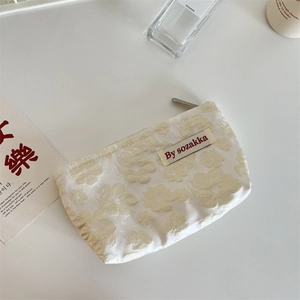 Macro shot of cream floral embossed makeup bag with delicate jacquard texture and label