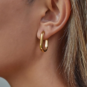 Close-up of gold oval hoop earrings showing smooth metallic texture on model's ear
