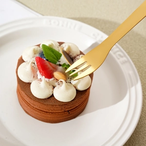 Golden stainless steel dessert fork piercing a chocolate cake with strawberries