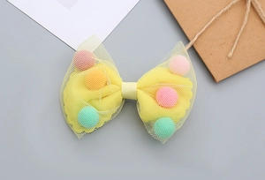 Close-up of a yellow mesh bow hair clip filled with colorful macaron pompoms