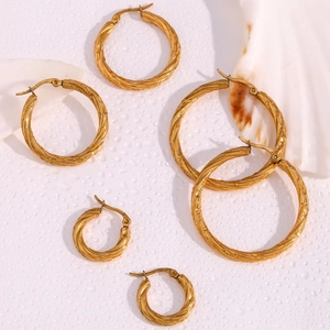 Detailed set of three twisted hoop earrings in gold finish on a shell background