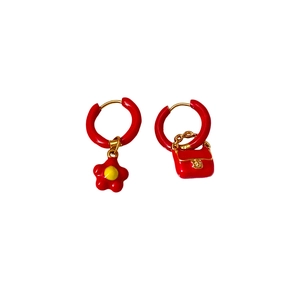 Asymmetric gold earrings with red flower and luxury handbag charms on white background