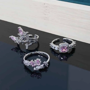 Detailed view of three silver rings with pink zircons and butterfly motifs on mirror surface