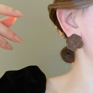 Macro shot of brown flocked camellia flower stud earrings with golden metallic accents