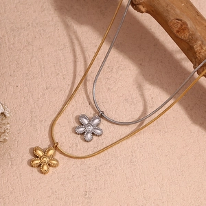 Detailed view of flower pendants on gold and silver snake chains over wooden accents