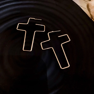 Gros plan de boucles d'oreilles croix dorées minimalistes sur un plateau noir