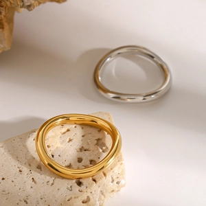 Detailed view of minimalist gold and silver wavy stainless steel rings on a stone surface