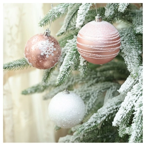 Detailed view of rose gold and white Christmas ornaments hanging on snowy pine branches
