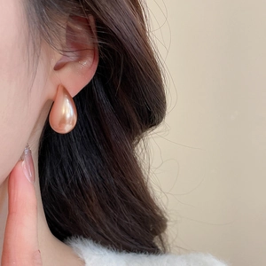 Close-up of minimalist teardrop earring with champagne pearl coating on model