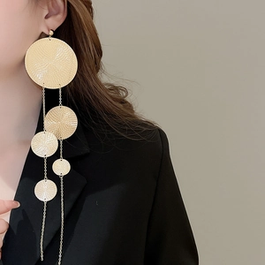 Detail of long gold tiered disc tassel earrings with hammered texture on a fashion model