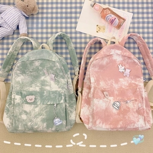 Detail of tie-dye canvas backpacks in mint and pink with cute plush animal pendants