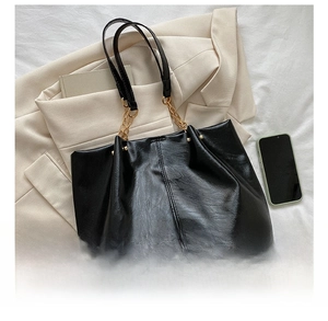 Détail d'un sac cabas noir avec texture litchi et bandoulière chaîne à côté d'un mobile