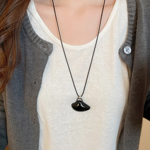 Detail of an irregular black stone pendant with a black cord on a casual outfit