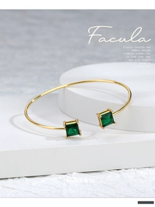 Macro detail of gold open cuff bracelet featuring square green zircon stones on display