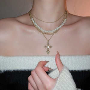 Detailed close-up of a layered gold necklace featuring pearls and a cross pendant on a model