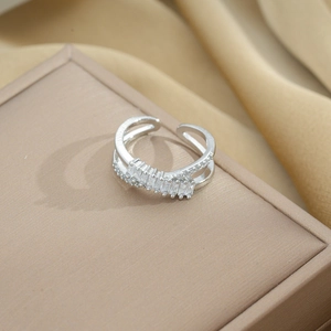 Macro view of adjustable silver cross ring with cubic zirconia on a beige jewelry display