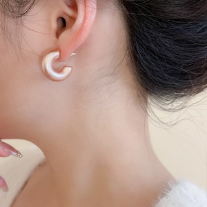 Close-up of champagne pink acrylic C-shaped earrings with a pearlescent glossy finish