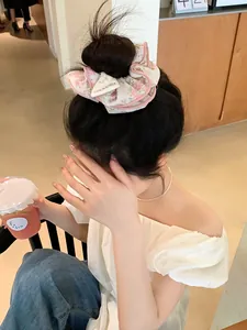 Floral fabric scrunchie with pink trim shown on a bun in a warm café setting