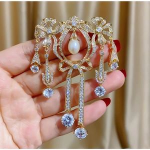 Détail d'une broche nœud dorée luxueuse avec zircons et gland de perles de nacre