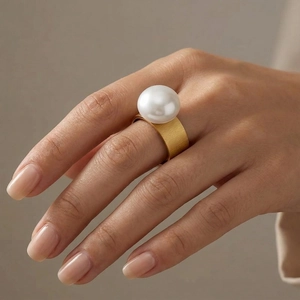 Macro view of wide gold brushed metal ring featuring a high-luster large white pearl