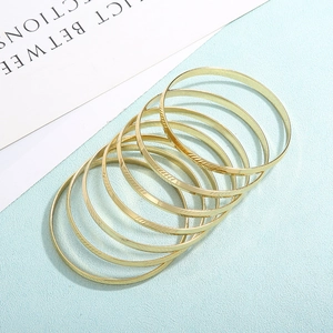 Primo piano di bracciali rigidi dorati impilabili con incisione testurizzata diagonale