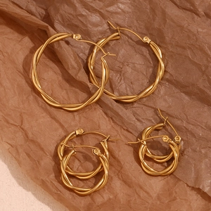 Detailed set of three sizes of gold-plated twisted hoop earrings on textured brown paper