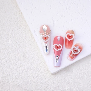 Detail of pink gradient press-on nails with pearls, rhinestones and red heart charms