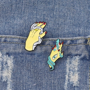 Enamel pins featuring a hand with a snake and a skeletal hand interlocking on denim jacket