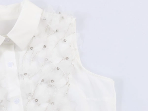 Détail d'un chemisier sans manches blanc avec tulle, strass argentés et perles brodées