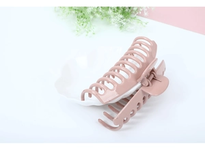 Detail of a large glossy pink hair claw clip displayed on a white shell plate