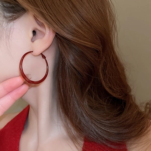 Macro shot of large red twist lacquer hoop earrings worn by a model in profile