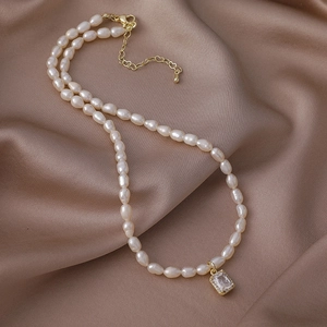 Detalle de collar de perlas de agua dulce con colgante de cristal sobre seda champán