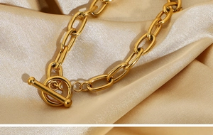 Macro shot of a golden paperclip link bracelet with OT toggle clasp on champagne silk fabric