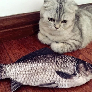 Realistic fish plush toy for cats on wooden floor with a grey striped cat sitting nearby