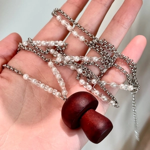 Détail du collier pendentif champignon en bois avec perles de cristal en main