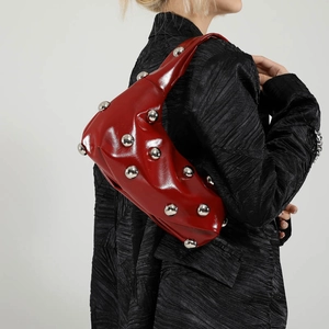 Red patent leather underarm bag with silver spherical studs worn with a black coat