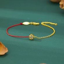 Detail of red rope and gold chain bracelet with a clear zircon on a green surface