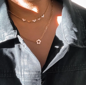 Close-up of layered 18k gold plated necklaces featuring heart charms and floral pendant