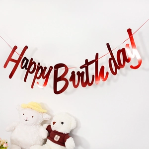 Detail of red metallic Happy Birthday banner on white wall with plush toys decoration