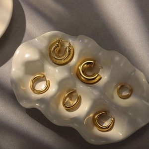 Detailed selection of golden stainless steel earrings on a textured ceramic tray