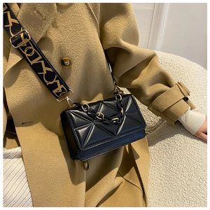 Detail of black quilted crossbody bag with stylish wide patterned strap and metal chain