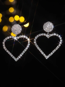 Macro close-up of silver heart earrings with sparkling rhinestones on dark background
